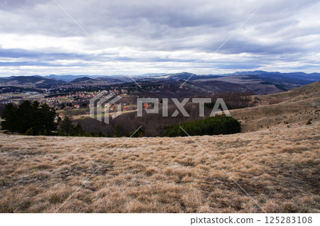 Scenic view of rolling hills and dense forest under a cloudy sky. The beauty of the natural landscape, with mountains visible in the distance Scenic view of rolling hills and dense forest under a cloudy sky. The beauty of the natural landscape, with mountains visible in the distance 125283108