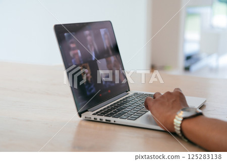 Photo of a laptop with modern headphones on a wooden table in a house with a modern interior.  125283138