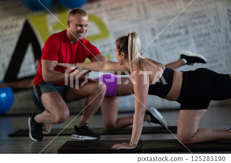 A trainer guides two women through stretching exercises in the gym, promoting flexibility, wellness, and a healthy lifestyle. 125283190