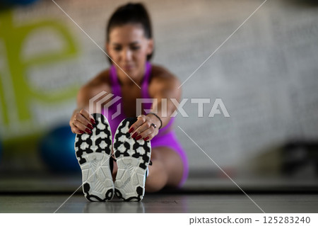 Woman Stretching in Gym. A athletic woman wearing a purple sports outfit is stretching her legs in a gym. 125283240