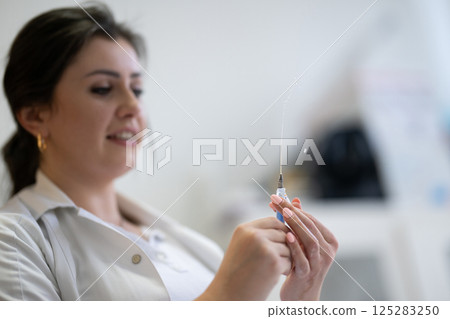 A focused nurse in a white lab coat carefully prepares a syringe for an injection in a professional healthcare environment. 125283250