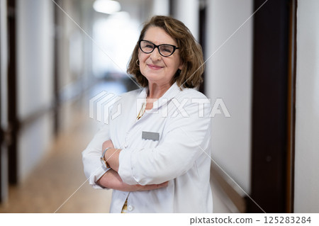 An experienced and confident elderly female doctor, wearing glasses and standing in the hospital hallway, embodies wisdom and dedication to patient care. An experienced and confident elderly female doctor, wearing glasses and standing in the hospital hallway, embodies wisdom and dedication to patient care. 125283284