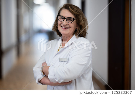 An experienced and confident elderly female doctor, wearing glasses and standing in the hospital hallway, embodies wisdom and dedication to patient care. An experienced and confident elderly female doctor, wearing glasses and standing in the hospital hallway, embodies wisdom and dedication to patient care. 125283307