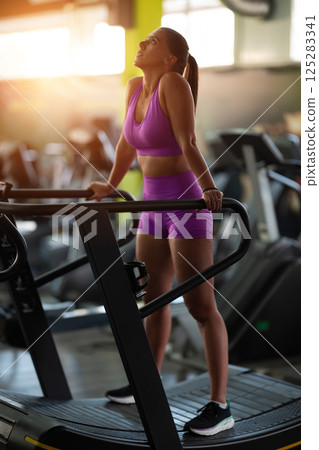 A fit woman resting after running on the treadmill and completing an intense conditioning workout, taking a moment to recover and recharge. 125283341