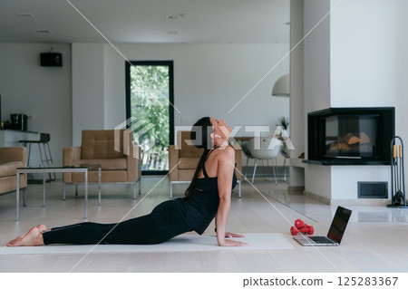 Young Beautiful Female Exercising, Stretching and Practising Yoga with Trainer via Video Call Conference in Bright Sunny House. Healthy Lifestyle, Wellbeing and Mindfulness Concept 125283367