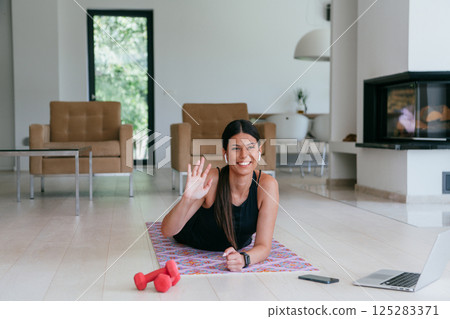 Young woman resting after online training while lying on the living room floor. 125283371