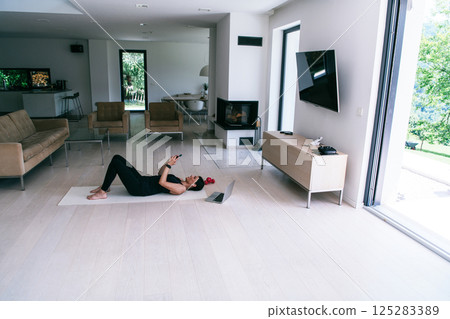 Sportswoman using a smartphone while resting and lying on the floor of modern house.  125283389