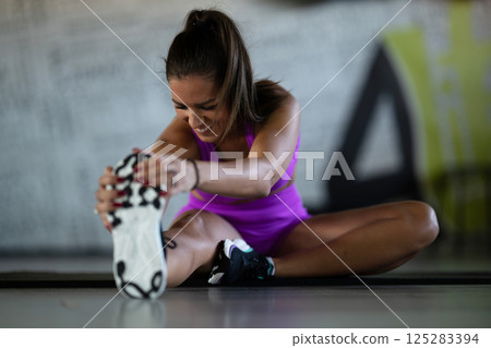 Woman Stretching in Gym. A athletic woman wearing a purple sports outfit is stretching her legs in a gym. Woman Stretching in Gym. A athletic woman wearing a purple sports outfit is stretching her legs in a gym. 125283394