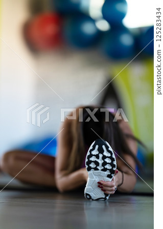 Woman Stretching in Gym. A athletic woman wearing a purple sports outfit is stretching her legs in a gym. 125283434