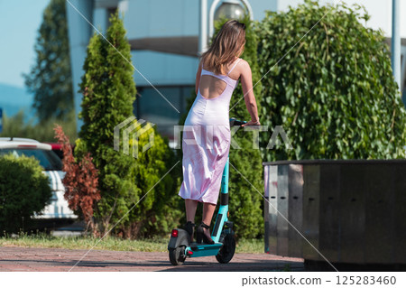 Elegant woman in a pink dress and sunglasses riding an electric scooter through the sunny city streets, embracing the freedom and style of a perfect urban adventure. Elegant woman in a pink dress and sunglasses riding an electric scooter through the sunny city streets, embracing the freedom and style of a perfect urban adventure. 125283460