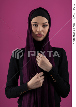 Beautiful Muslim woman in a hijab posing elegantly in a studio with a pink background. 125283537