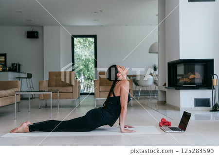 Young Beautiful Female Exercising, Stretching and Practising Yoga with Trainer via Video Call Conference in Bright Sunny House. Healthy Lifestyle, Wellbeing and Mindfulness Concept 125283590