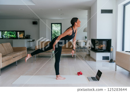 Young Beautiful Female Exercising, Stretching and Practising Yoga with Trainer via Video Call Conference in Bright Sunny House. Healthy Lifestyle, Wellbeing and Mindfulness Concept 125283644