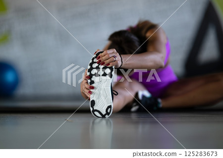 Woman Stretching in Gym. A athletic woman wearing a purple sports outfit is stretching her legs in a gym. 125283673