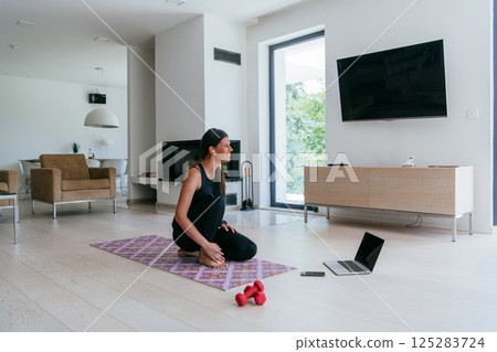 Young Beautiful Female Exercising, Stretching and Practising Yoga with Trainer via Video Call Conference in Bright Sunny House. Healthy Lifestyle, Wellbeing and Mindfulness Concept 125283724