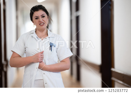 A dedicated nurse in uniform walks briskly down a well-lit hospital corridor, reflecting professionalism and urgency in a healthcare setting. 125283772