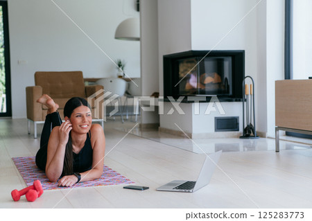 Young woman resting after online training while lying on the living room floor. 125283773