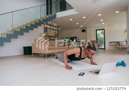 Training At Home. Sporty african american man doing the training while watching an online tutorial on a laptop, exercising in the living room, free space.  125283774