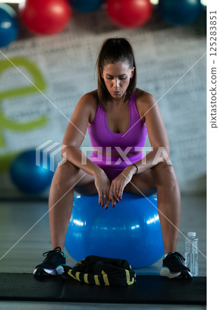 A fit woman takes a well deserved break in the gym, sipping water from her bottle after an intense workout session 125283851