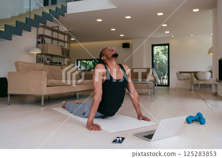 Training At Home. Sporty african american man doing the training while watching an online tutorial on a laptop, exercising in the living room, free space.  125283853