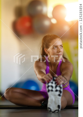 Woman Stretching in Gym. A athletic woman wearing a purple sports outfit is stretching her legs in a gym. 125283854