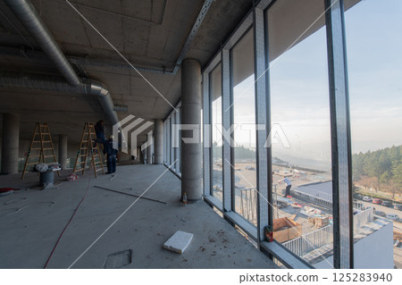 A captivating view of a modern business building under construction, showcasing its raw industrial interior with exposed steel beams and concrete walls bathed in the warm, golden hues of a sunset A captivating view of a modern business building under construction, showcasing its raw industrial interior with exposed steel beams and concrete walls bathed in the warm, golden hues of a sunset 125283940