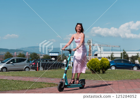 Elegant woman in a pink dress and sunglasses riding an electric scooter through the sunny city streets, embracing the freedom and style of a perfect urban adventure. 125284052