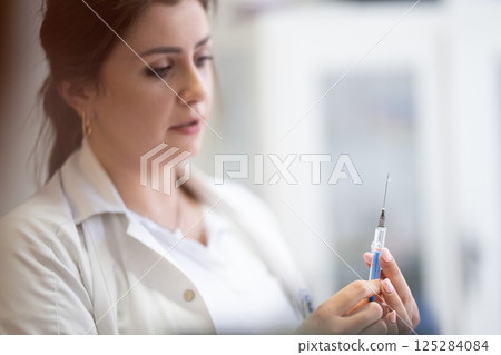 A focused nurse in a white lab coat carefully prepares a syringe for an injection in a professional healthcare environment. A focused nurse in a white lab coat carefully prepares a syringe for an injection in a professional healthcare environment. 125284084
