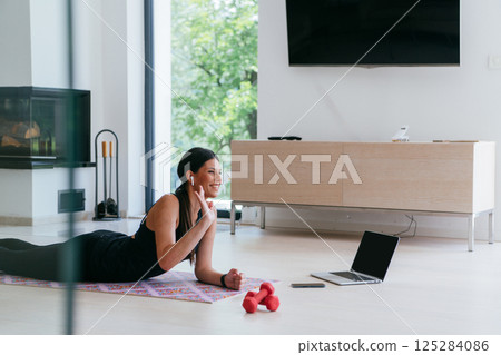 Young woman resting after online training while lying on the living room floor. 125284086