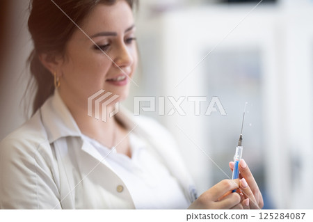 A focused nurse in a white lab coat carefully prepares a syringe for an injection in a professional healthcare environment. 125284087