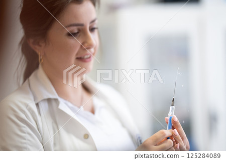 A focused nurse in a white lab coat carefully prepares a syringe for an injection in a professional healthcare environment. A focused nurse in a white lab coat carefully prepares a syringe for an injection in a professional healthcare environment. 125284089