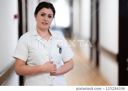 A dedicated nurse in uniform walks briskly down a well-lit hospital corridor, reflecting professionalism and urgency in a healthcare setting. 125284106