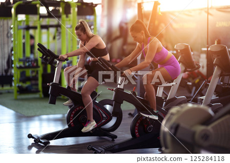 Two fitness women working together on a conditioning workout in the gym, supporting each other with strength, focus, and determination. 125284118