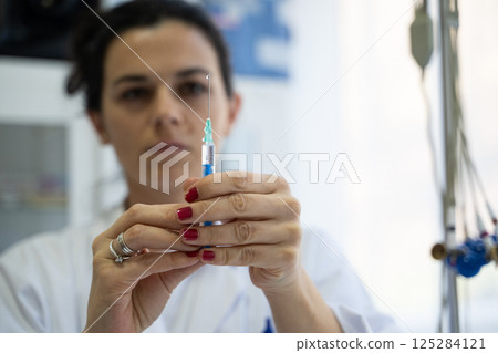 A focused nurse in a white lab coat carefully prepares a syringe for an injection in a professional healthcare environment. 125284121