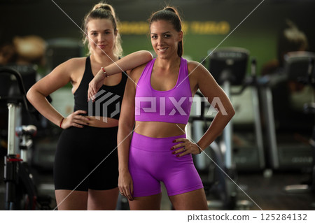 Two fitness women resting and recovering in the gym after an intense workout session, showcasing strength, endurance, and dedication to their fitness journey. Two fitness women resting and recovering in the gym after an intense workout session, showcasing strength, endurance, and dedication to their fitness journey. 125284132