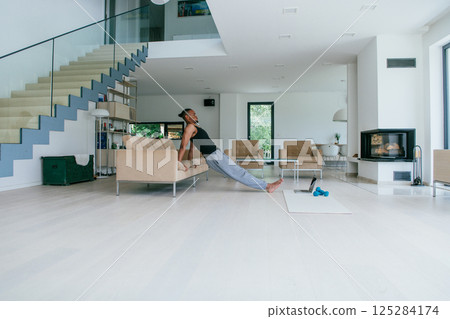 Training At Home. Sporty man doing the training while watching an online tutorial on a laptop, exercising in the living room, free space. 125284174