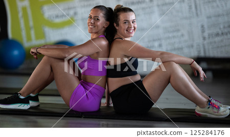 Two fitness women resting and recovering in the gym after an intense workout session, showcasing strength, endurance, and dedication to their fitness journey. Two fitness women resting and recovering in the gym after an intense workout session, showcasing strength, endurance, and dedication to their fitness journey. 125284176