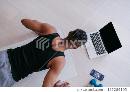 Training At Home. Sporty man doing the training while watching an online tutorial on a laptop, exercising in the living room, free space. Training At Home. Sporty man doing the training while watching an online tutorial on a laptop, exercising in the living room, free space. 125284195