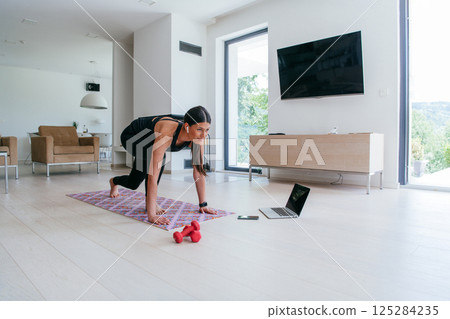 Young Beautiful Female Exercising, Stretching and Practising Yoga with Trainer via Video Call Conference in Bright Sunny House. Healthy Lifestyle, Wellbeing and Mindfulness Concept 125284235