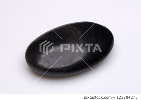 Smooth, polished black river stone isolated on a plain white background showcasing its organic shape and reflective surface Smooth, polished black river stone isolated on a plain white background showcasing its organic shape and reflective surface 125284275