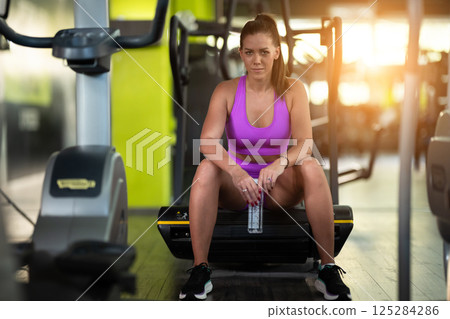A fit woman takes a well deserved break in the gym, sipping water from her bottle after an intense workout session 125284286