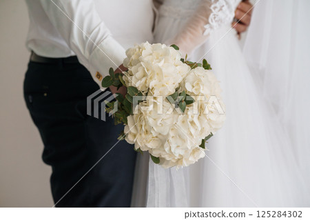 Capturing Wedding Embrace and Bouquet: A Moment of Intimacy with Groom Holding Bride's Flowers, Soft White Hydrangeas, Classic Bridal Style, and Navy Accents, Symbolizing Love and Unity 125284302