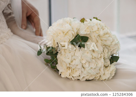 Elegant Bridal Bouquet and Dress Detail Reflecting Wedding Day Sophistication in a Brightly Lit Interior Setting Elegant Bridal Bouquet and Dress Detail Reflecting Wedding Day Sophistication in a Brightly Lit Interior Setting 125284306