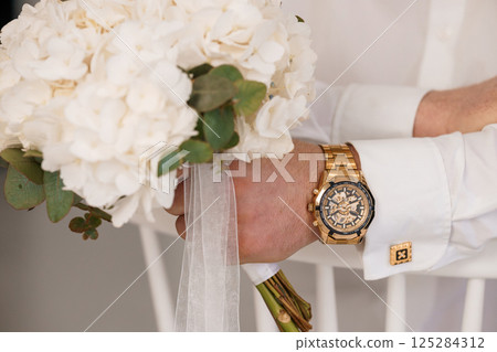 Wedding details featuring a glamorous gold skeleton watch resting against a lush bridal bouquet and a sharply dressed groom's attire, symbolizing wealth and sophistication Wedding details featuring a glamorous gold skeleton watch resting against a lush bridal bouquet and a sharply dressed groom's attire, symbolizing wealth and sophistication 125284312