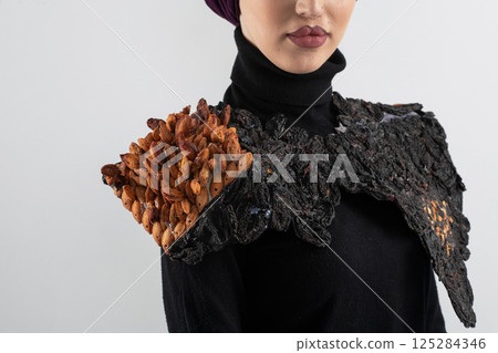 A stylish Muslim woman in a hijab presents her innovative handmade fashion accessory crafted from dried plums in a professional studio. A stylish Muslim woman in a hijab presents her innovative handmade fashion accessory crafted from dried plums in a professional studio. 125284346