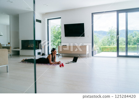 Young woman resting after online training while lying on the living room floor. 125284420