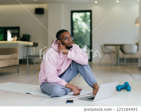 African American man in glasses sitting at a table in a modern living room, using a laptop for business video chat, conversation with friends and entertainment. African American man in glasses sitting at a table in a modern living room, using a laptop for business video chat, conversation with friends and entertainment. 125284491