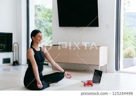 Young Beautiful Female Exercising, Stretching and Practising Yoga with Trainer via Video Call Conference in Bright Sunny House. Healthy Lifestyle, Wellbeing and Mindfulness Concept Young Beautiful Female Exercising, Stretching and Practising Yoga with Trainer via Video Call Conference in Bright Sunny House. Healthy Lifestyle, Wellbeing and Mindfulness Concept 125284499