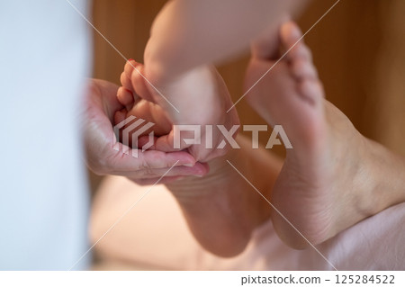 Foot Massage Therapy in a Relaxing Spa Setting. A professional massage therapist in a white uniform provides a soothing foot massage to a client in a calm and serene spa environment Foot Massage Therapy in a Relaxing Spa Setting. A professional massage therapist in a white uniform provides a soothing foot massage to a client in a calm and serene spa environment 125284522