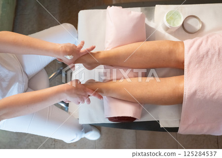 Foot Massage Therapy in a Relaxing Spa Setting. A professional massage therapist in a white uniform provides a soothing foot massage to a client in a calm and serene spa environment 125284537